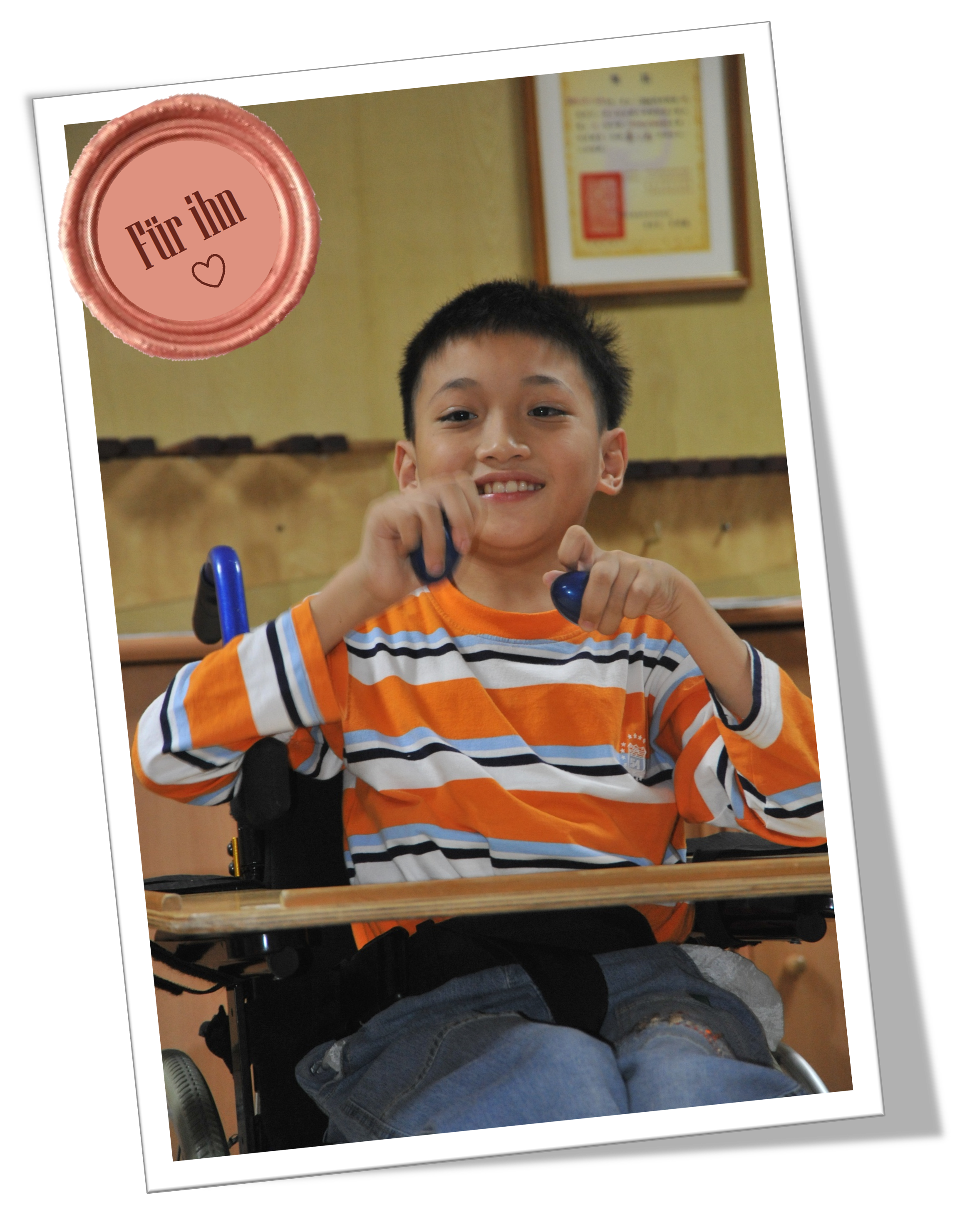 Ein asiatischer Junge im Rollstuhl mit Rasseln lächelt in die Kamera.